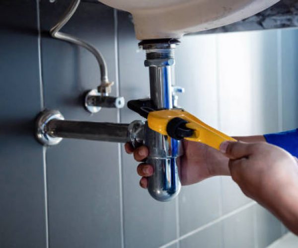 Plumber fixing white sink pipe with adjustable wrench.
